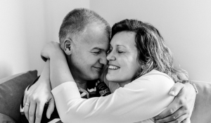 A couple sitting on a sofa, smiling and embracing with their eyes closed — a tender moment of love, calm, and connection.